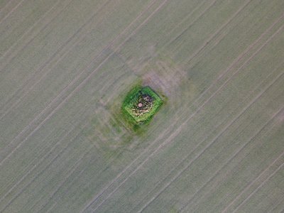 crop field from above with lines in crop. in middle is metal circle, stones, and a unfarmed square.