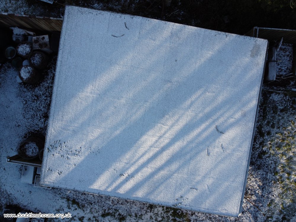 Snow on outbuilding roof, from above. With lines of shadow and light from trees.