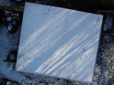 Snow on outbuilding roof, from above. With lines of shadow and light from trees.