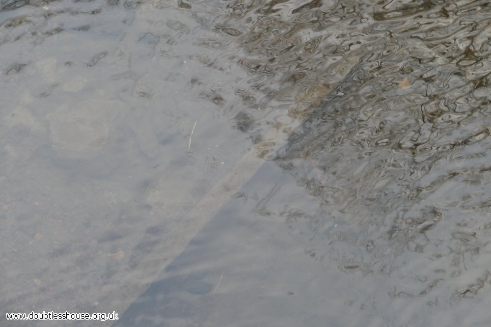 water, with reflections on it and a post and stones underneath